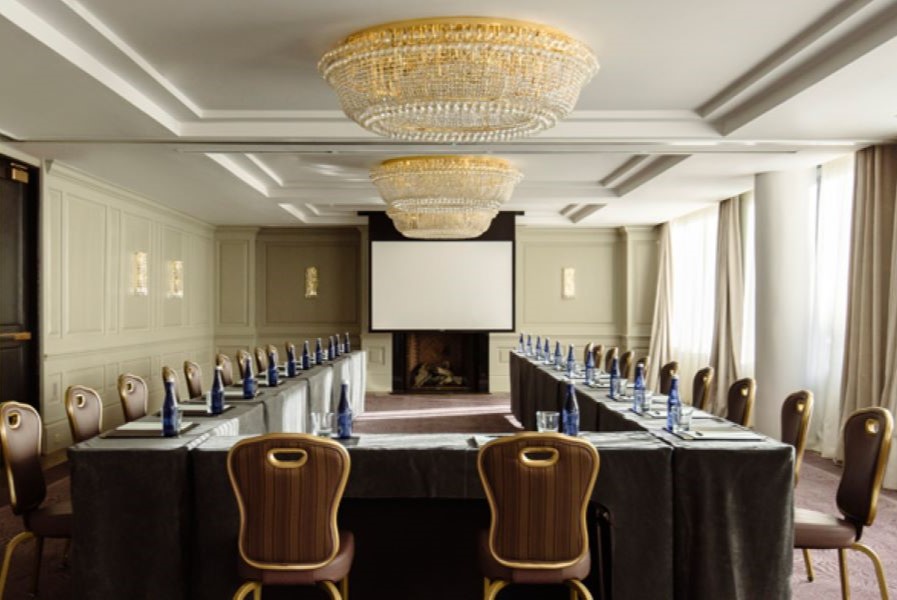 A refined and intimate conference room at the Dupont Circle Hotel, featuring a U-shaped table setup, luxurious chandeliers, and soft natural light from large windows, creating a sophisticated meeting space.