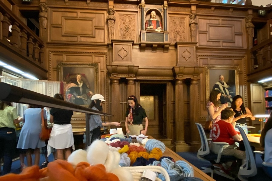 A group of people engaged in a craft activity in a beautifully decorated library space with large portraits and shelves of books.