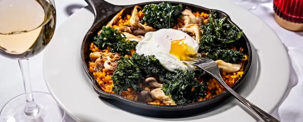 skillet with paella, kale and fresh egg on a white table spread